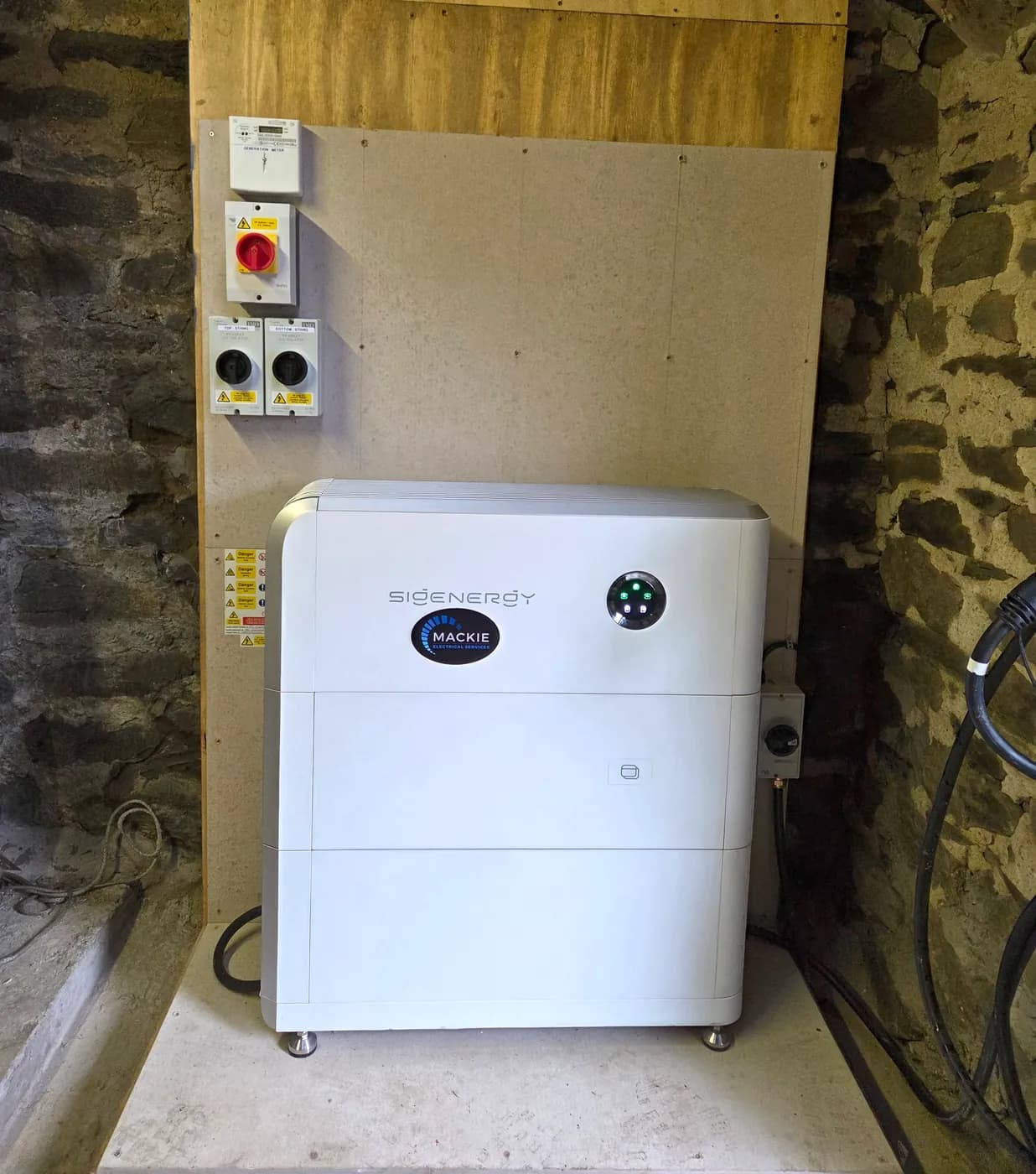 Sigenergy battery storage and labelled string isolators installed in a stone outbuilding at Kinlochard